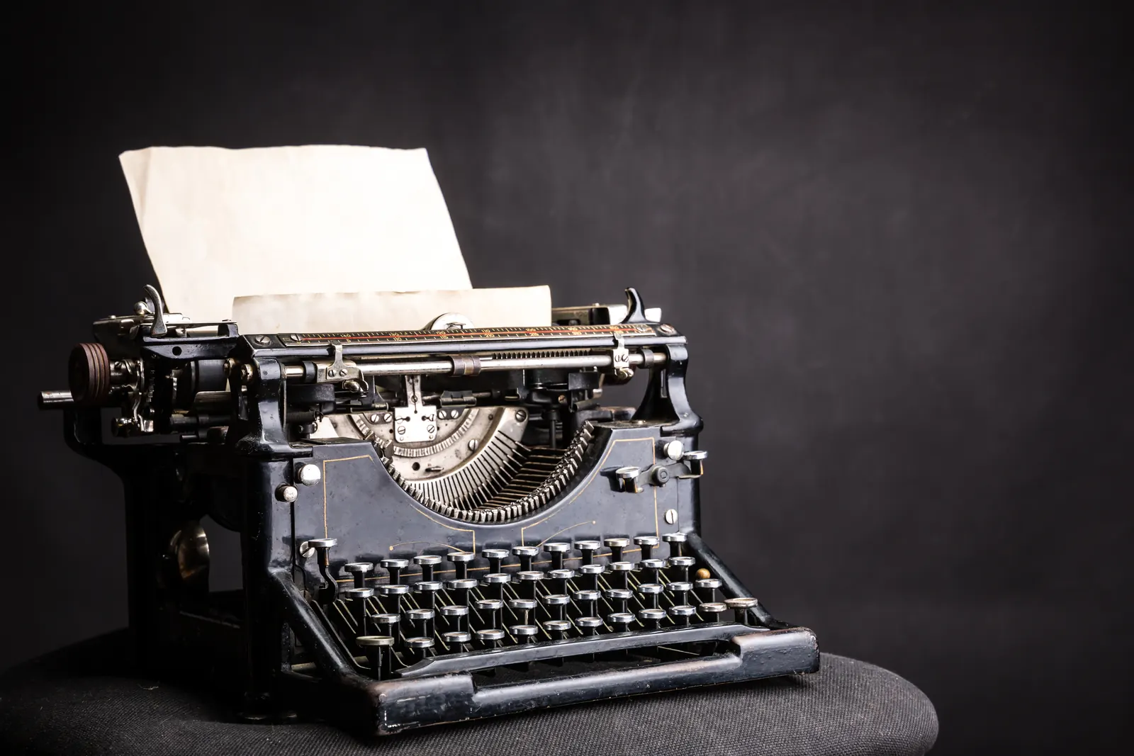 An antique black typewriter with a blank sheet of paper in it, against a dark background