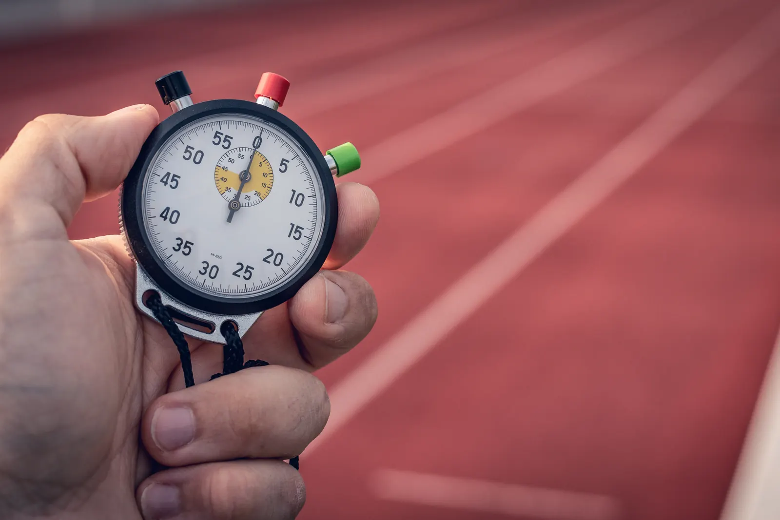 A hand holds an analog stopwatch above a red running track