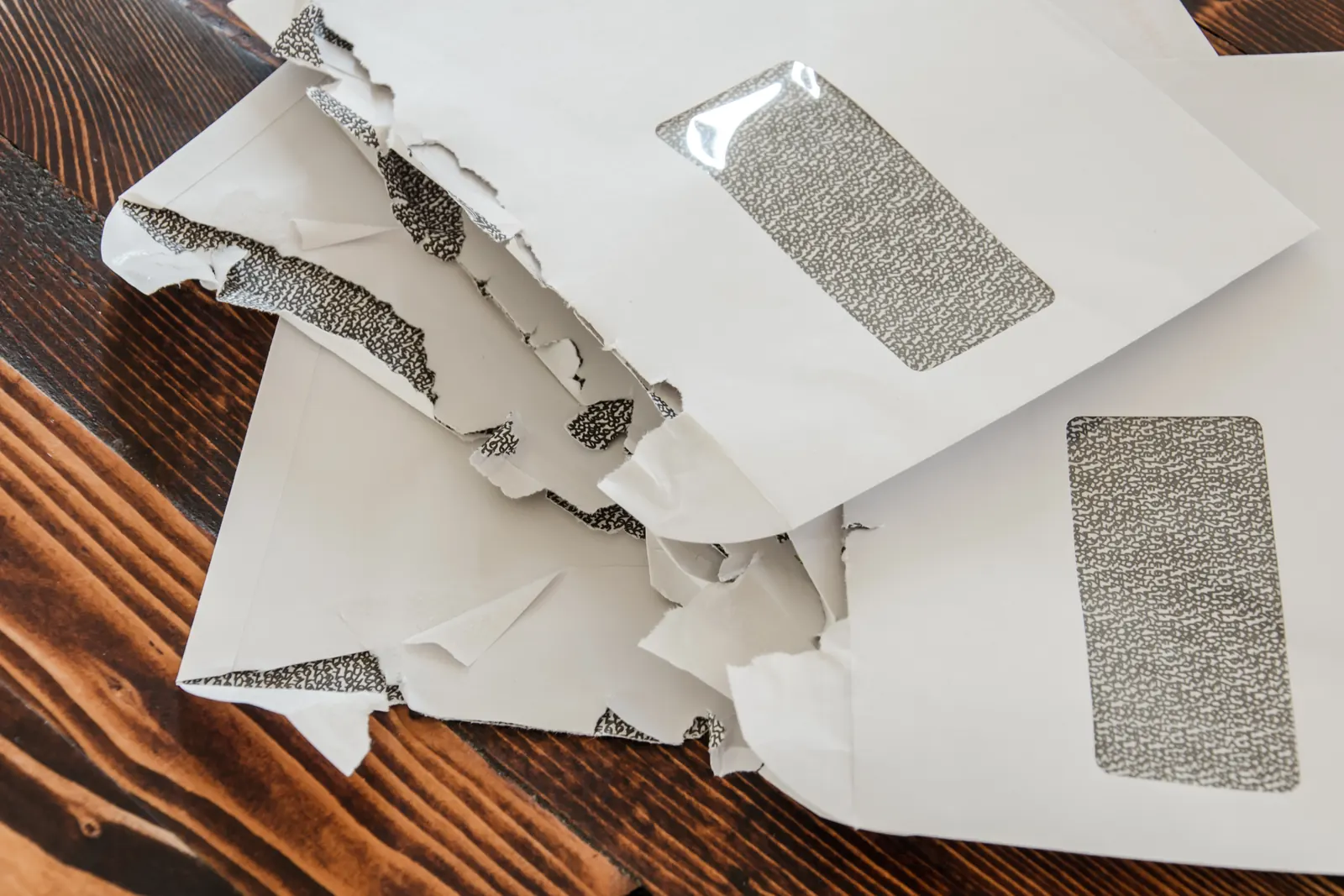 Several torn-open white window envelopes lying on a dark wooden table