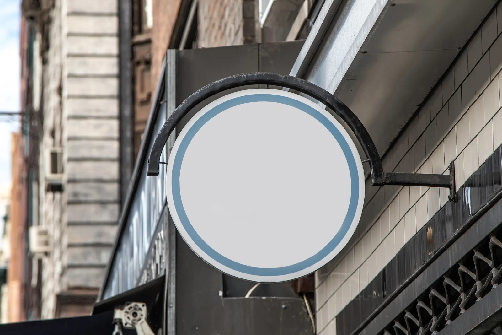A blank round sign on a curved iron bracket over a shop entrance on a city street