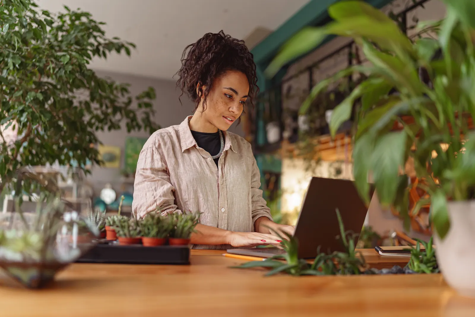 A florist working on a laptop at the counter of her shop, surrounded by plants