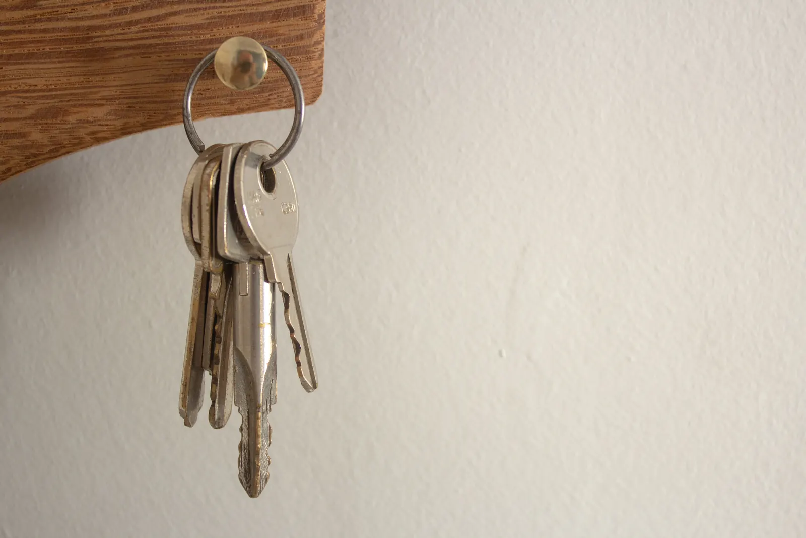 A ring of keys hanging from a brass peg under a wooden shelf, against a plain white wall