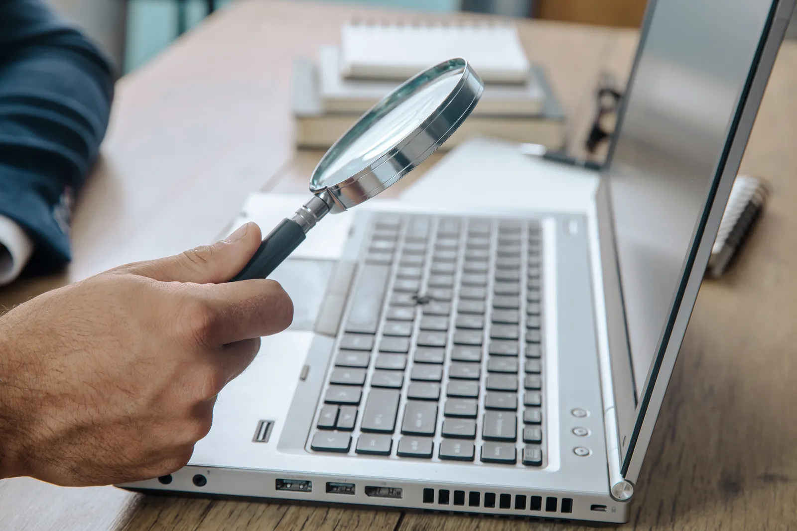 A hand holds a magnifying glass over a laptop keyboard