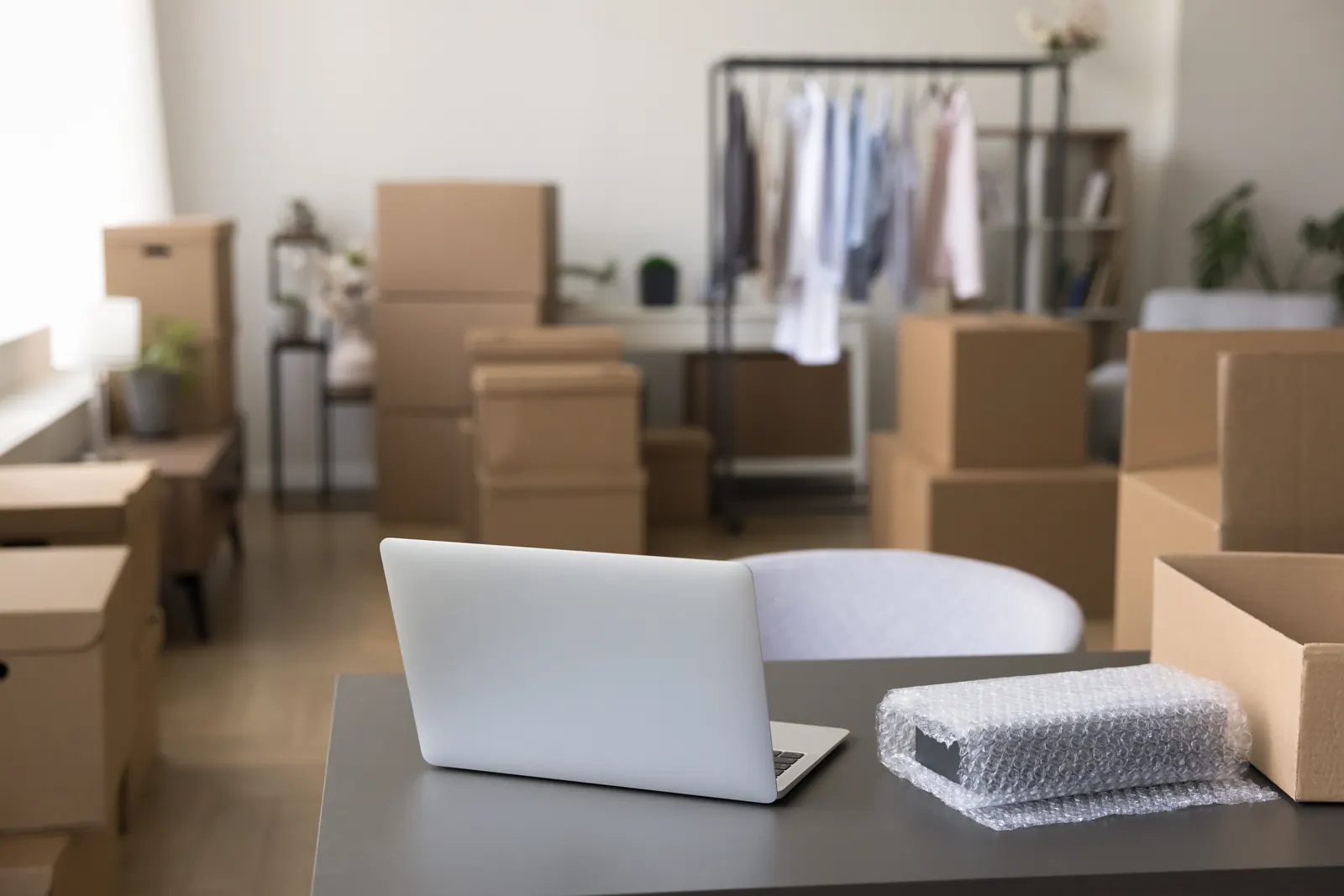 Cardboard boxes stacked around a half-unpacked shop, with a rack of clothes at the back and a laptop on a desk in front