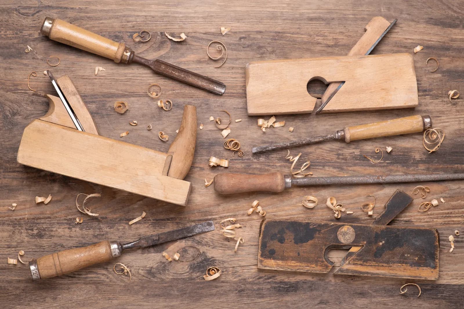 Old wooden hand planes and chisels laid out on a wooden workbench among curls of wood shavings
