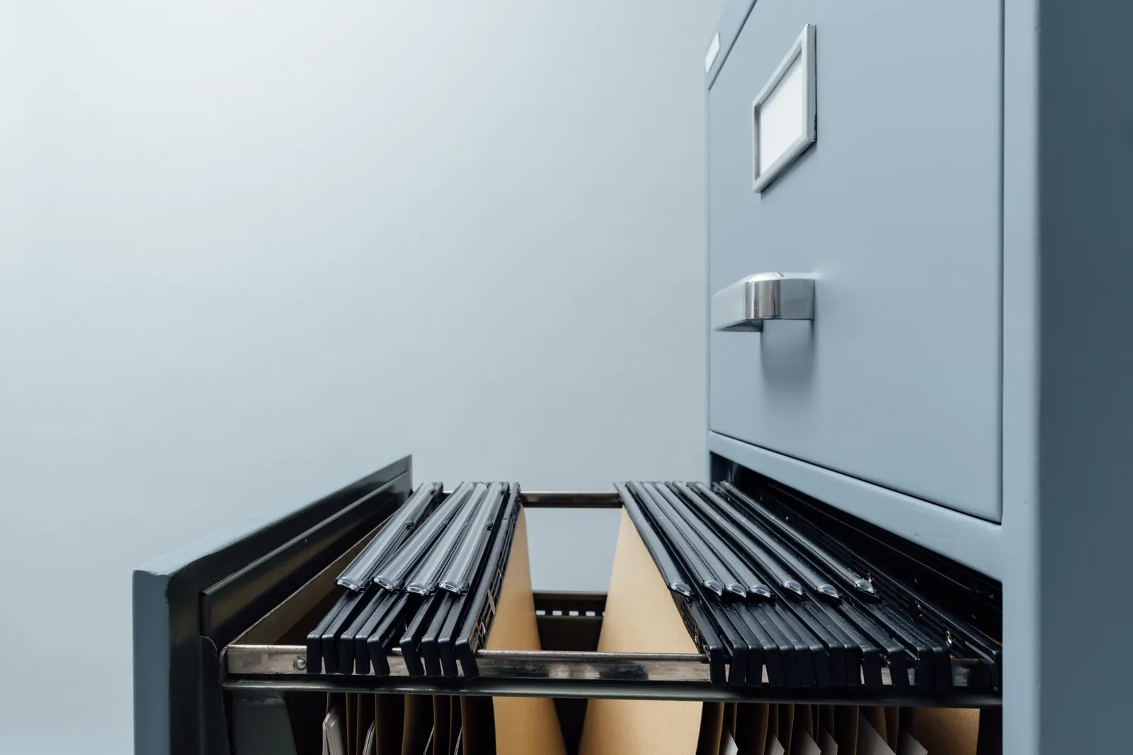 An open grey filing cabinet drawer of hanging file folders, with a gap between two groups of files