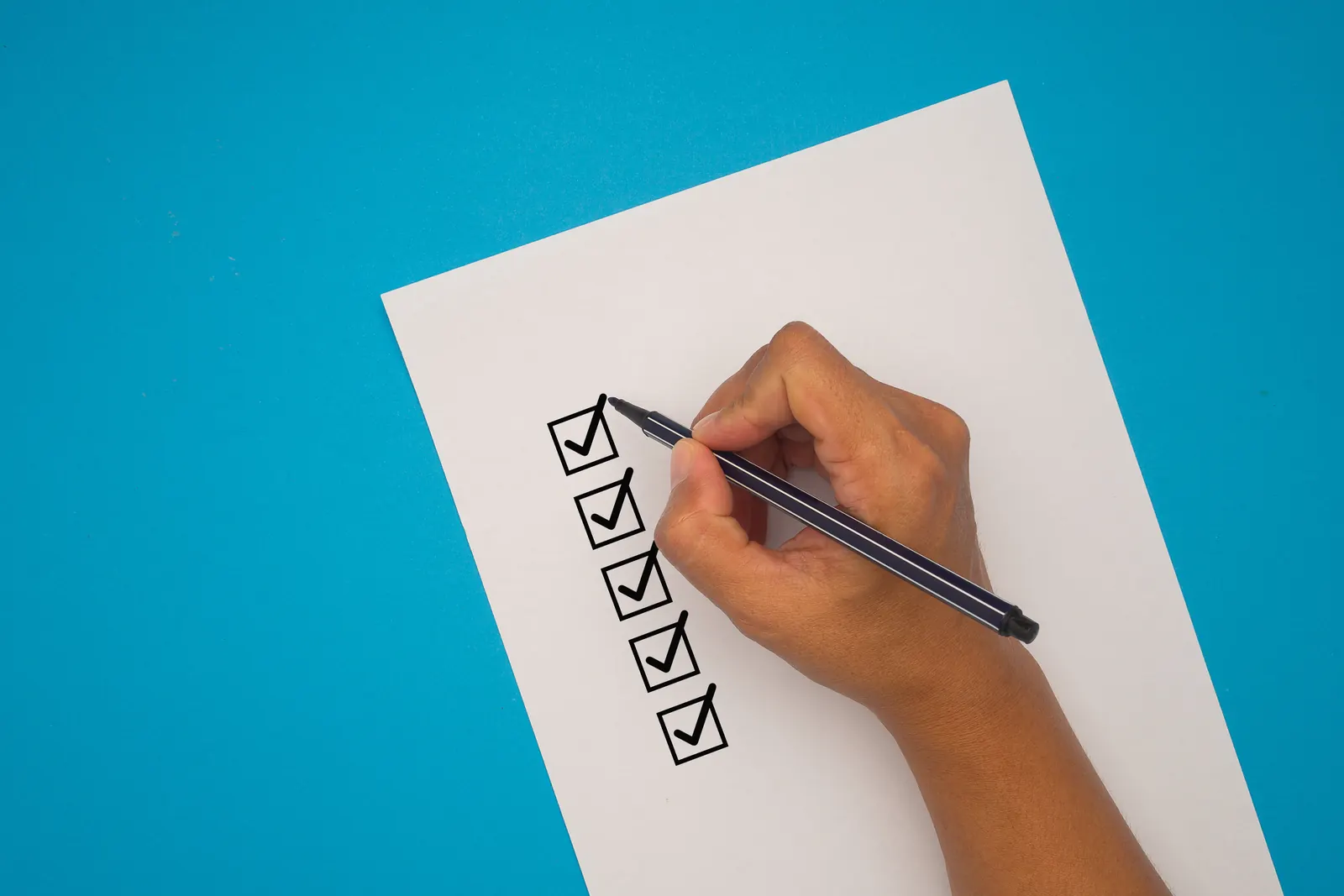 A hand ticking a column of boxes on a sheet of paper, on a blue background