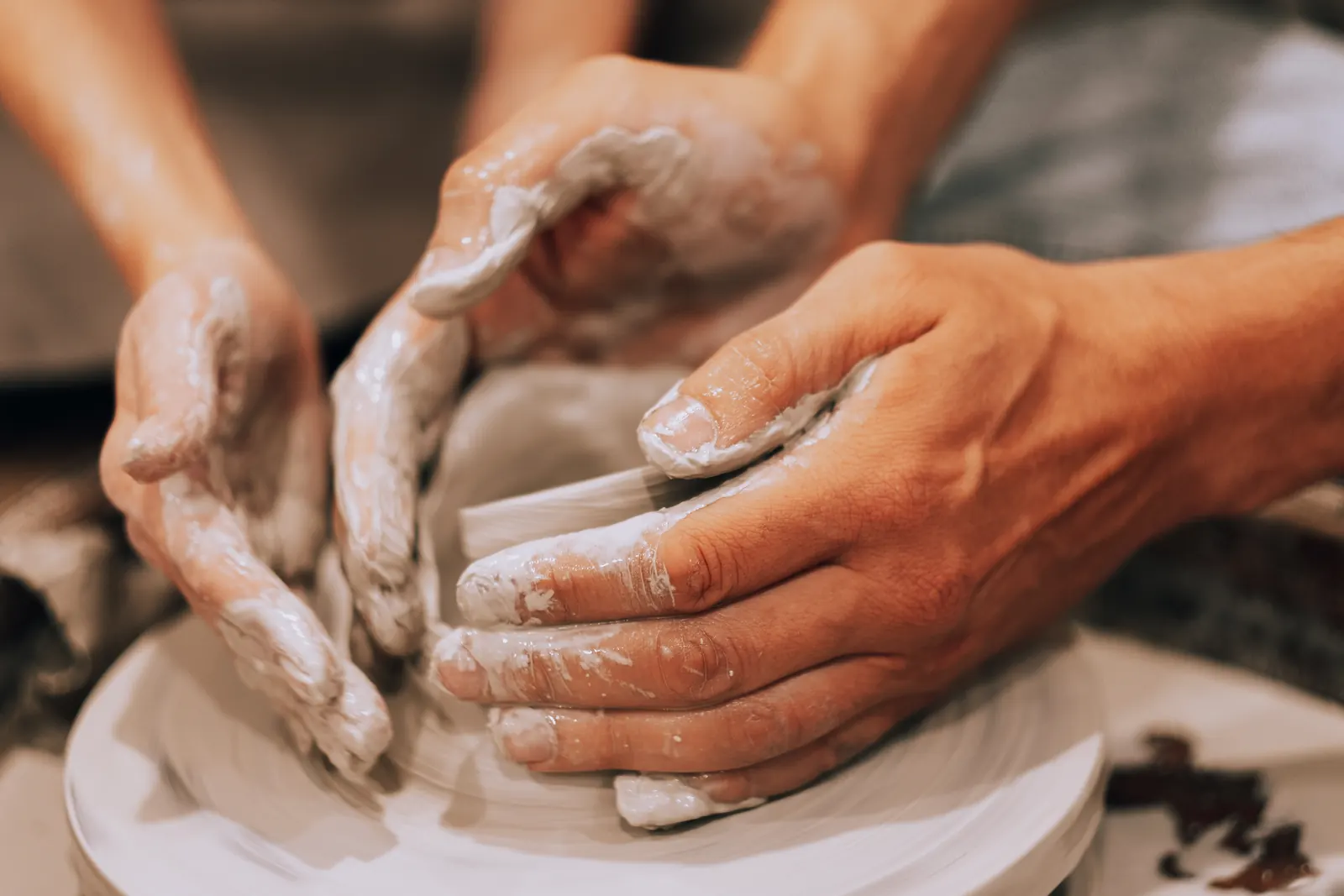 Close-up of two pairs of clay-covered hands shaping a pot together on a potter's wheel